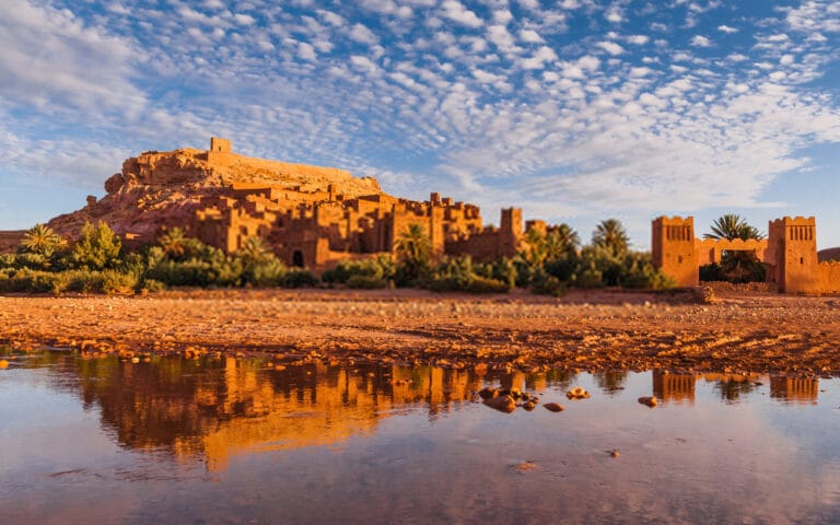 Ait Benhaddou Morocco kasbah reflected in water at sunrise with dramatic clouds