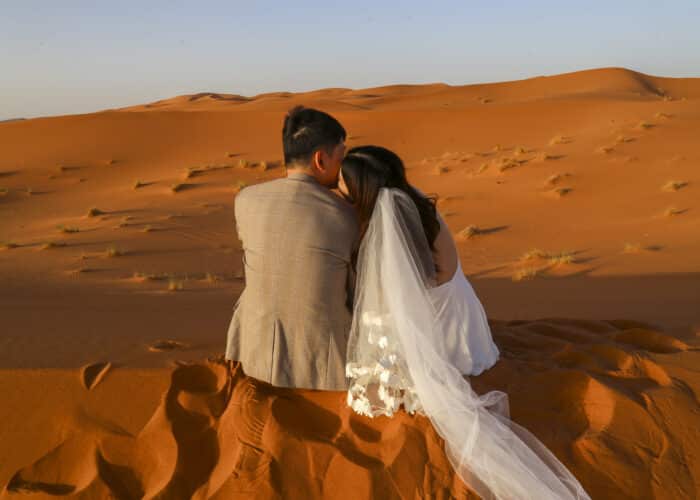 Couple in wedding attire watching sunset in Merzouga dunes during 7 Day Morocco Tour from Marrakech to Merzouga back to Casablanca