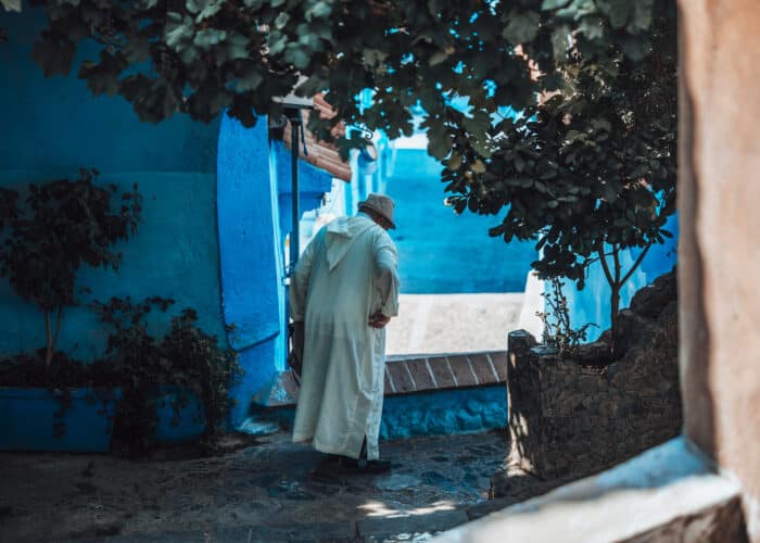 Elderly Moroccan man in djellaba walking in blue alley.