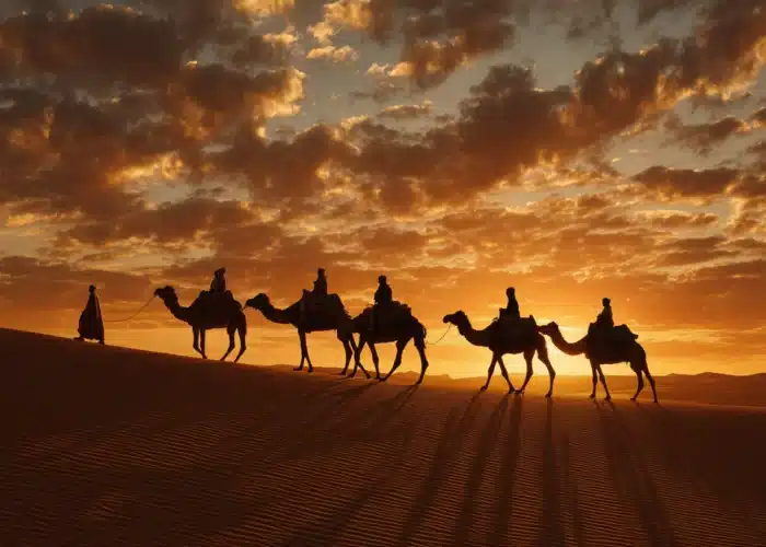 Merzouga camel ride at sunset in the Moroccan Sahara Desert with caravan silhouettes